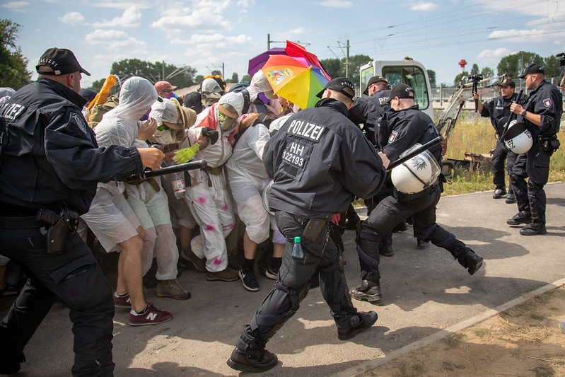 Blockade of a finger meets the police, an umbrella in rainbow colors can be seen.